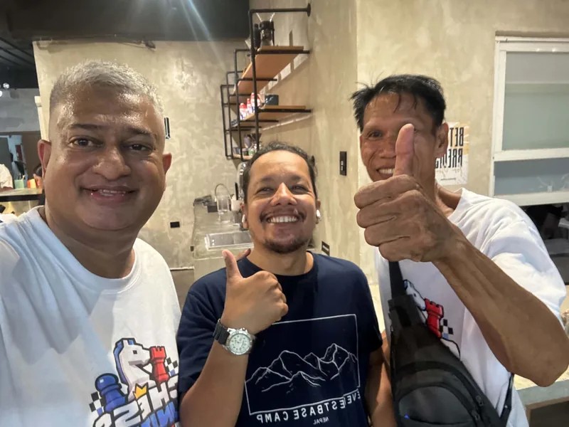 Three people posing together at a restaurant, with a Chess United shirt in the middle.