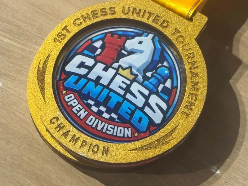 Close-up of the gold Chess United Tournament 1.0 medal for the Open Division champion, with its red, white and blue ribbon.
