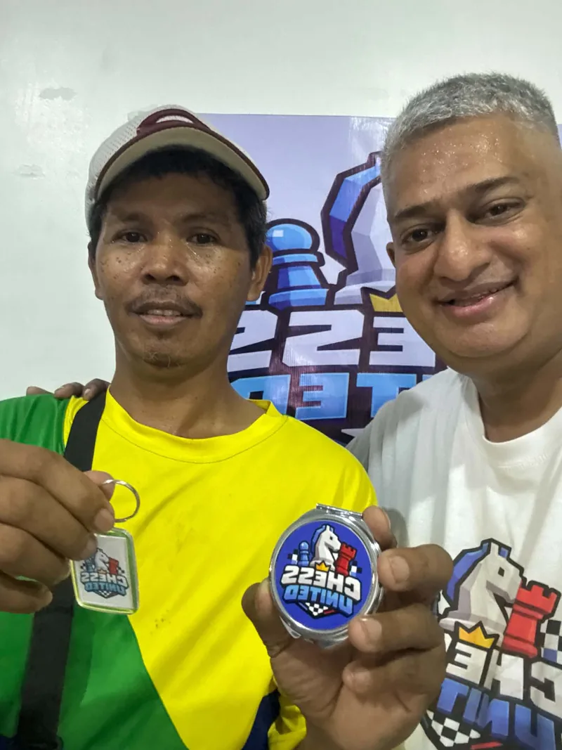 Two Chess United members holding up a club pin and a keychain in front of the club backdrop.