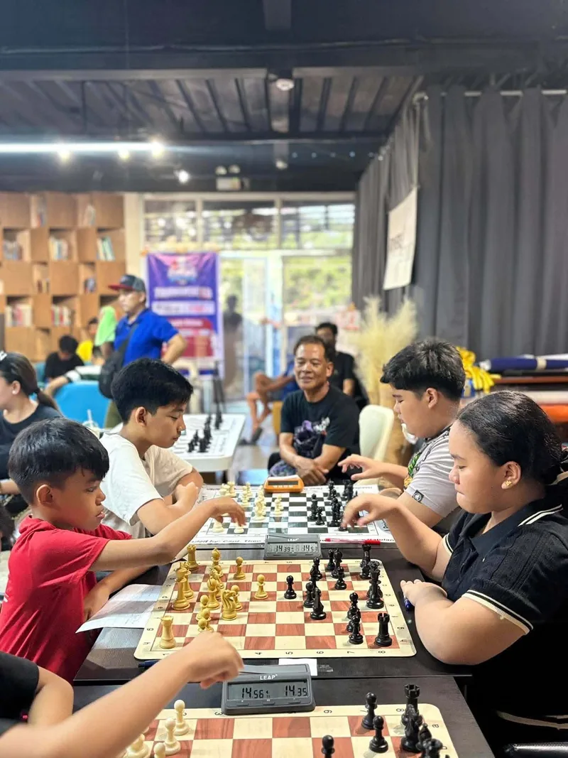 A full tournament hall at Rovers Coffee during Chess United Tournament 1.0, with players at every table and warm pendant lights overhead.
